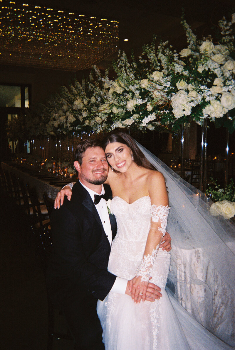 Film photo of bride sitting in groom's lap at reception table
