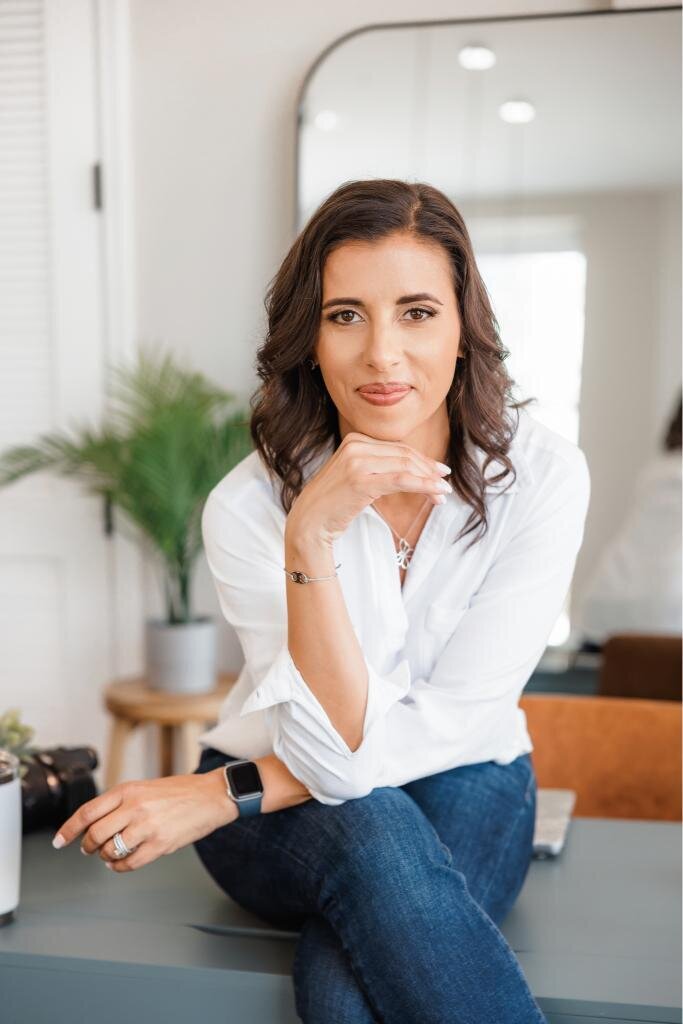 Jo, the founder of Branding by Jo sitting on a desk with her hand under her chin for a lifestyle headshot during her brand session at a studio in Orlando.