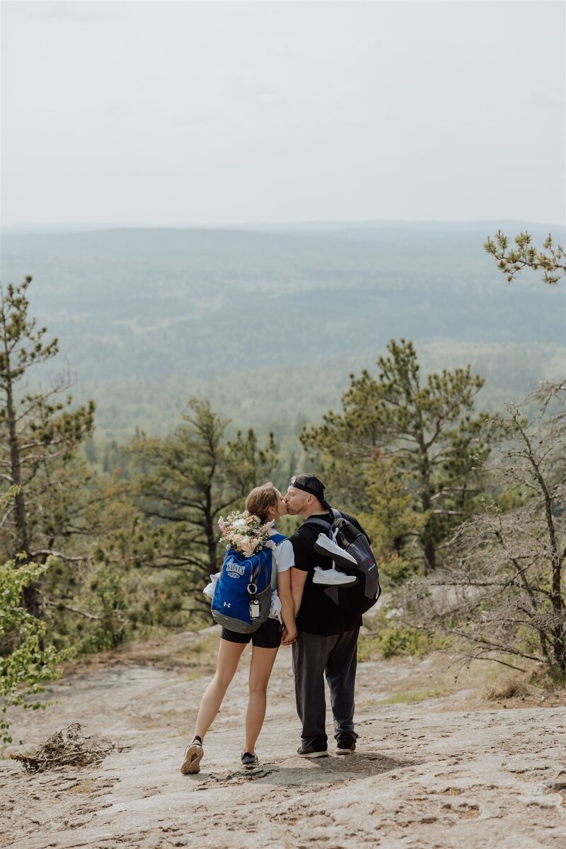 couple wearing hiking backpacks and kissing while hiking to the elopement destination