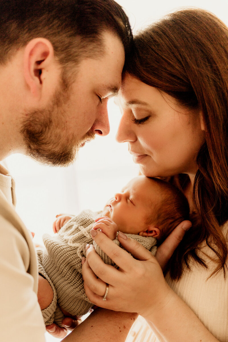 Mother and father peer down at their newborn baby boy who is wearing a sage sweater.