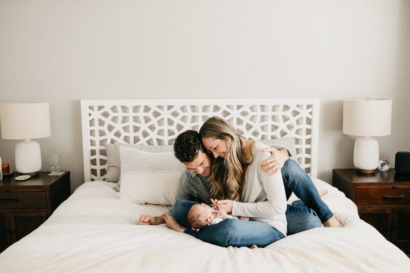 family with newborn baby sitting on a bed looking at the baby while smiling