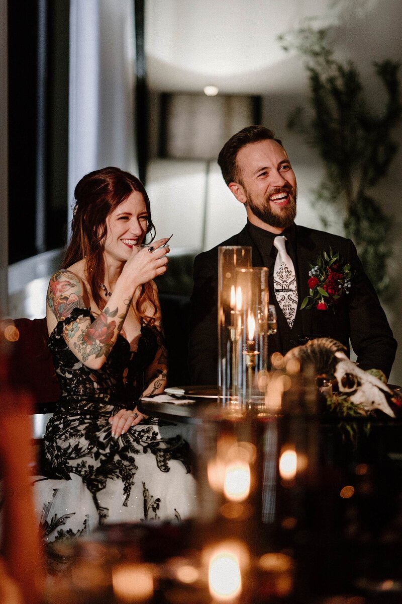A couple sitting at a wedding reception table laughing 