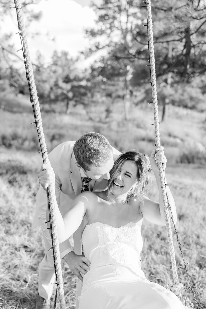 Smiling bride and groom swinging on a rustic swing at their August wedding in Franktown, Colorado, capturing a playful and romantic moment in a picturesque outdoor setting