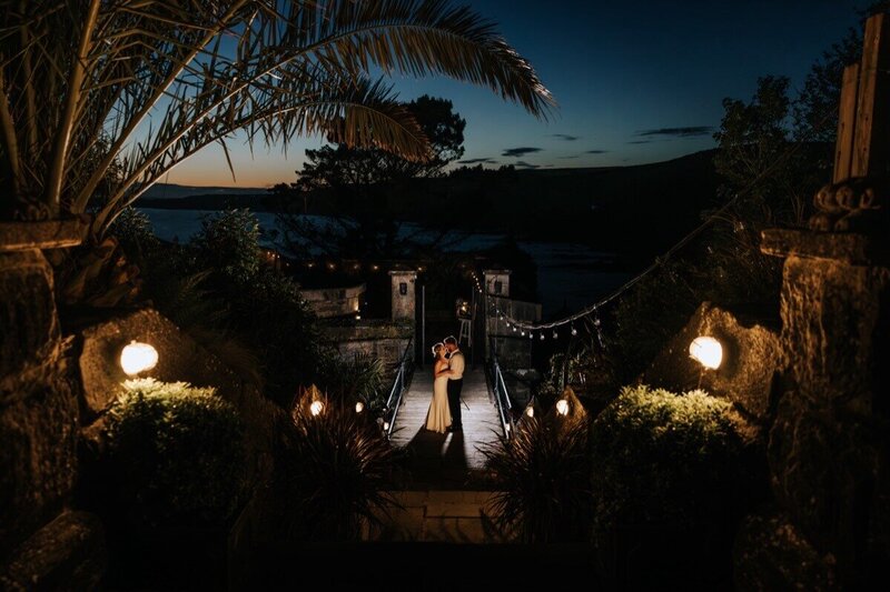 A bride and groom kissing at night  surrounded by lights and nature