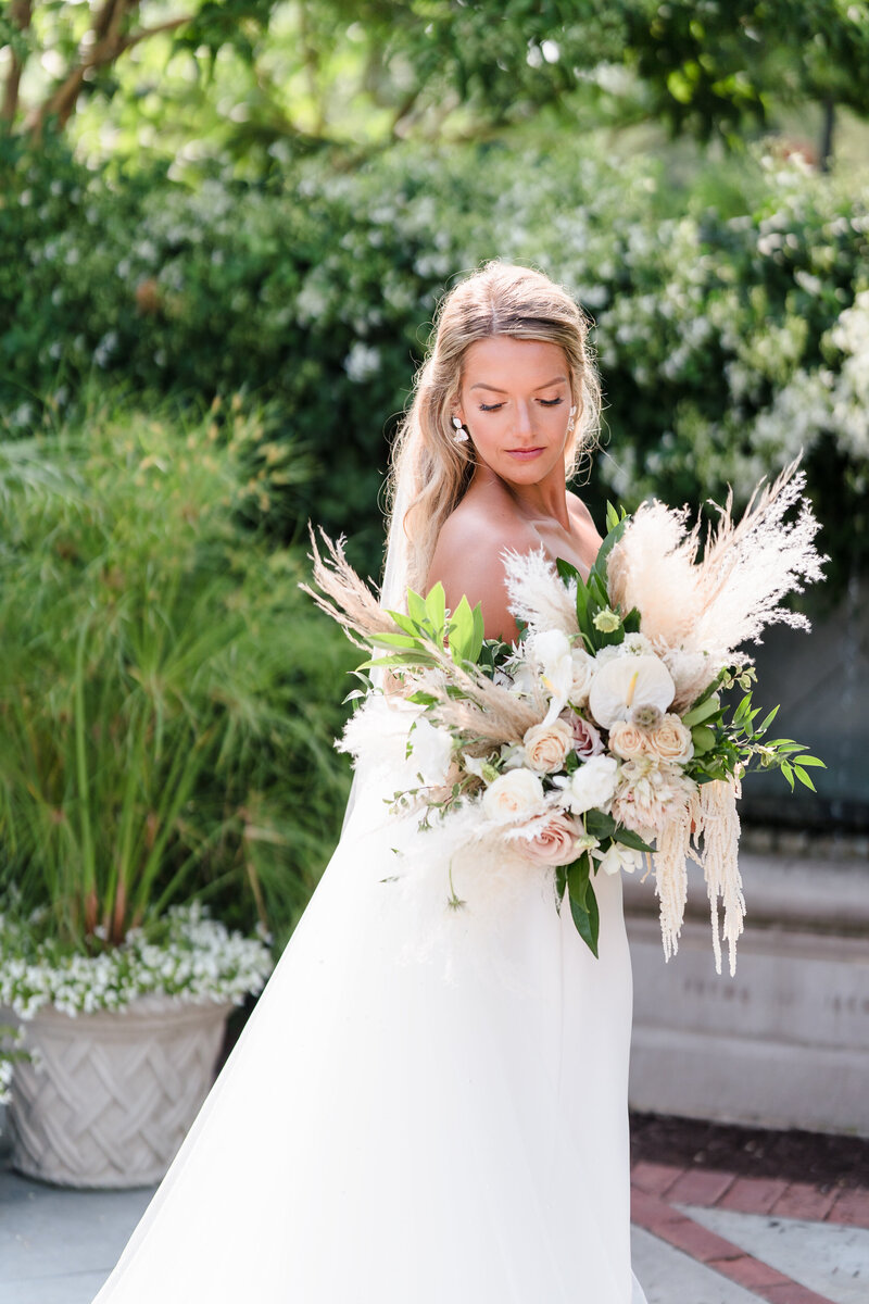 A bride gazes at her large boho bouquet while standing in the gardens at the Franklin Park Conservatory