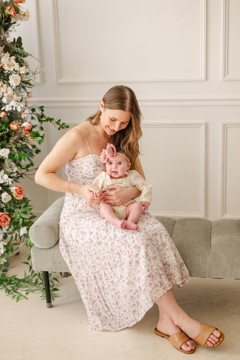 Mom holding her baby during a studio mini session, surrounded by soft floral accents.