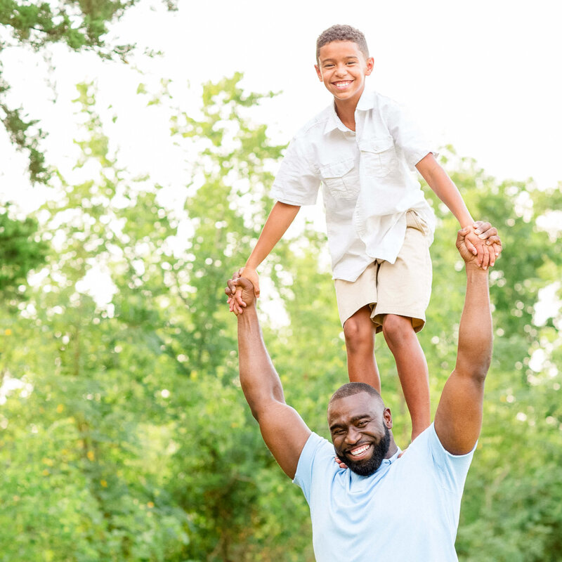 Father holding son on shoulders holding hands in greenery