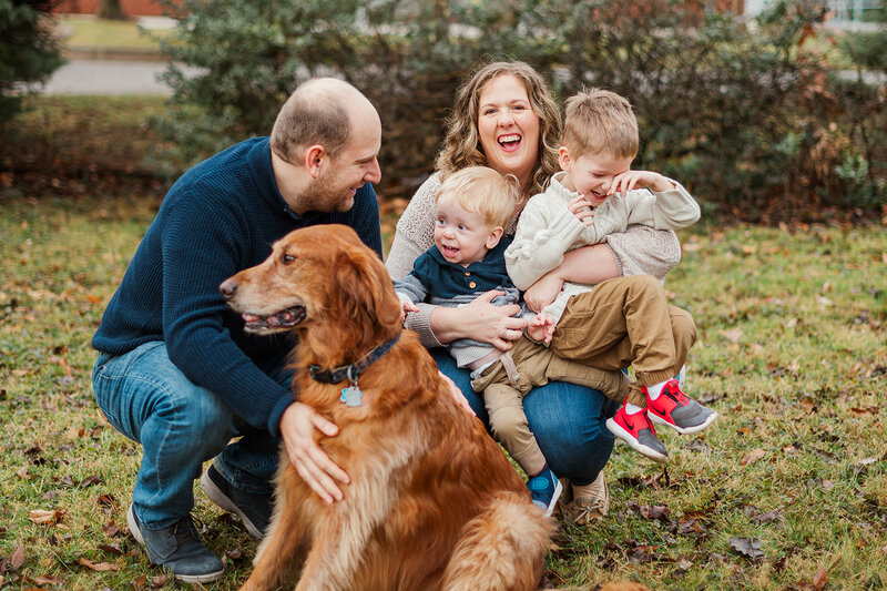 Mom and dad down on the ground with their two young boys playing and laughing with their golden retriever by york pa photographer