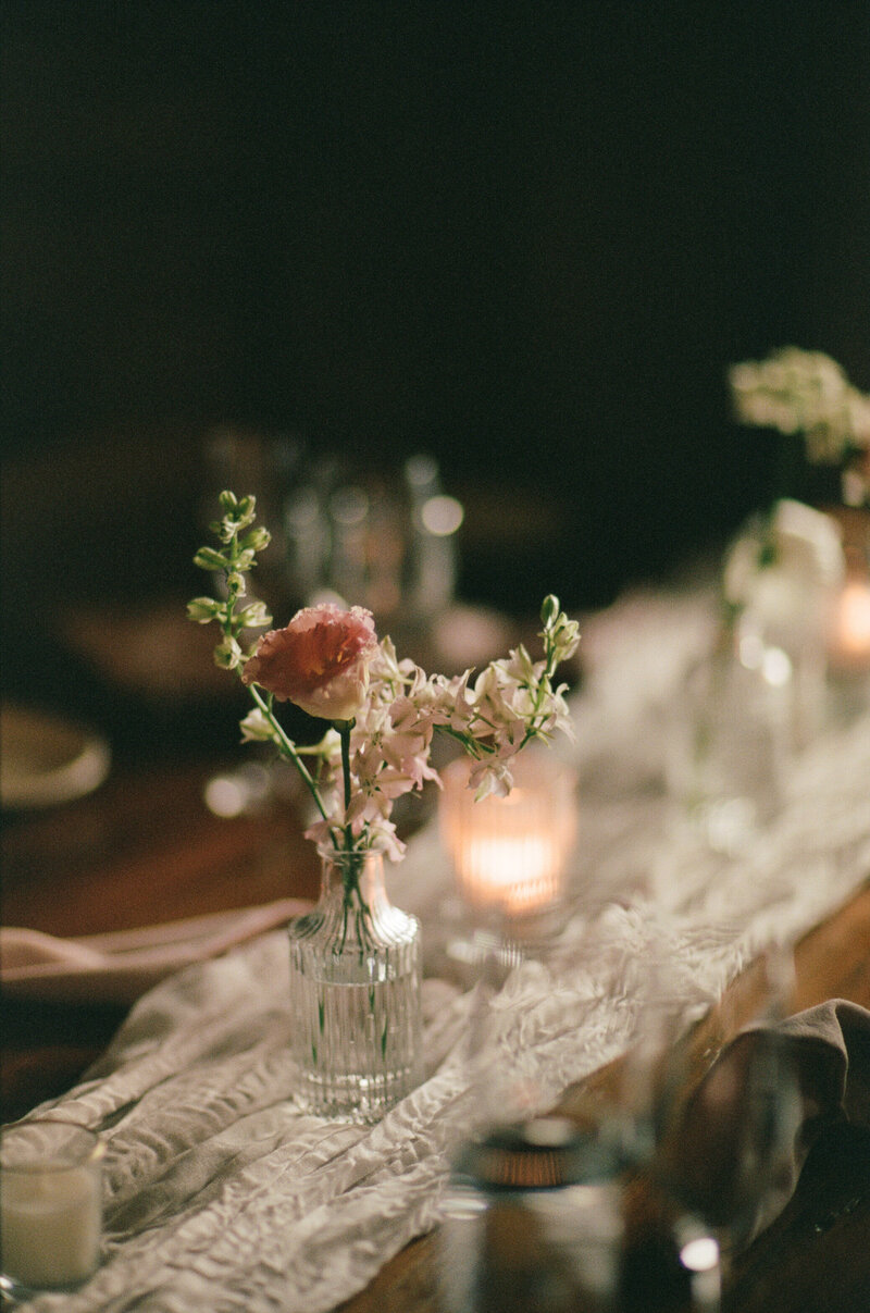A film photograph of a table adorned with a glass vase filled with flowers and lit candles, creating a warm ambiance.