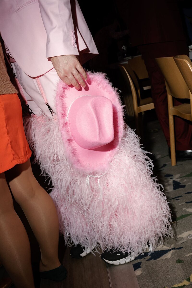Gay man in pink suit with feather chaps and feather brimmed pink cowboy hat at side 