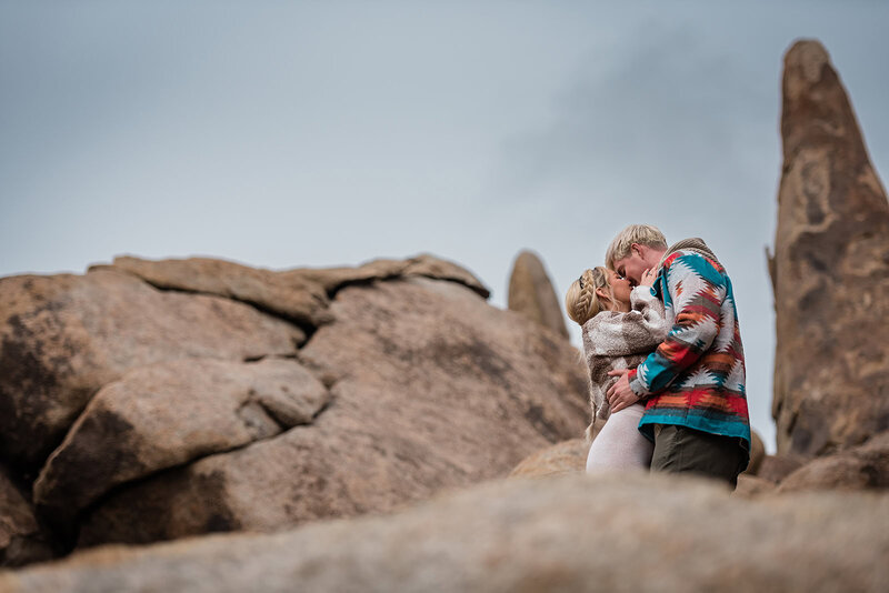 A photographer for luxury, multi-day elopements captures a couple in casual clothes kissing as they are exploring rounded rocks and hiking in California during their luxury destination elopement wedding.