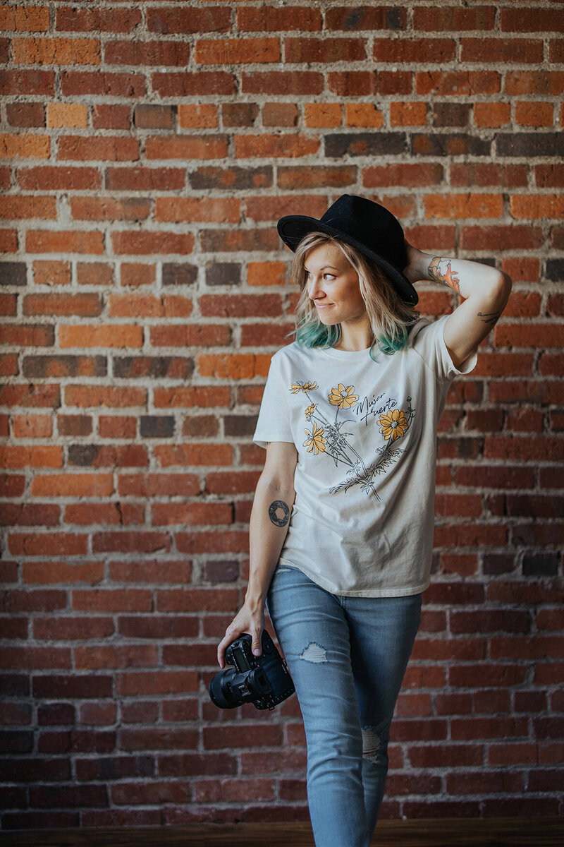 woman with camera in front of brick wall