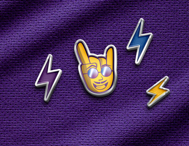 Four enamel pins placed on purple fabric. Three pins are a lighting bolt and the other is a rocker hand symbol with a smiling face wearing reflective sunglasses.
