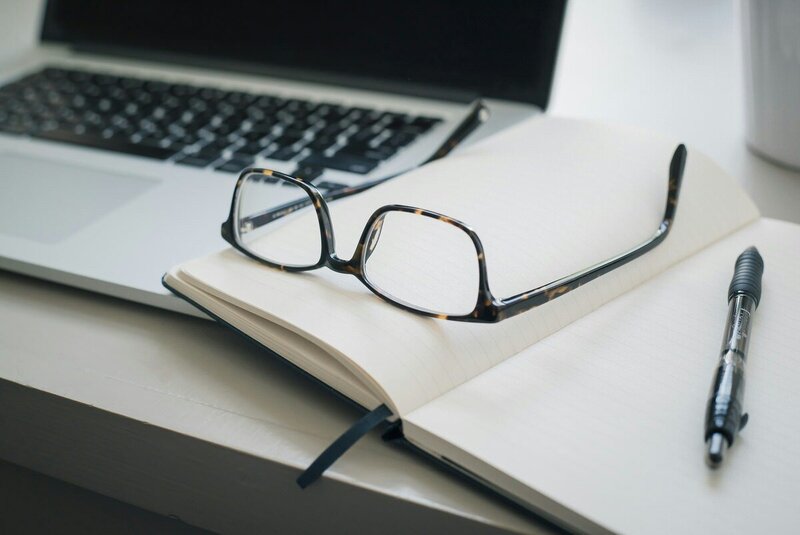 glasses sitting on open notebook  next to laptop computer