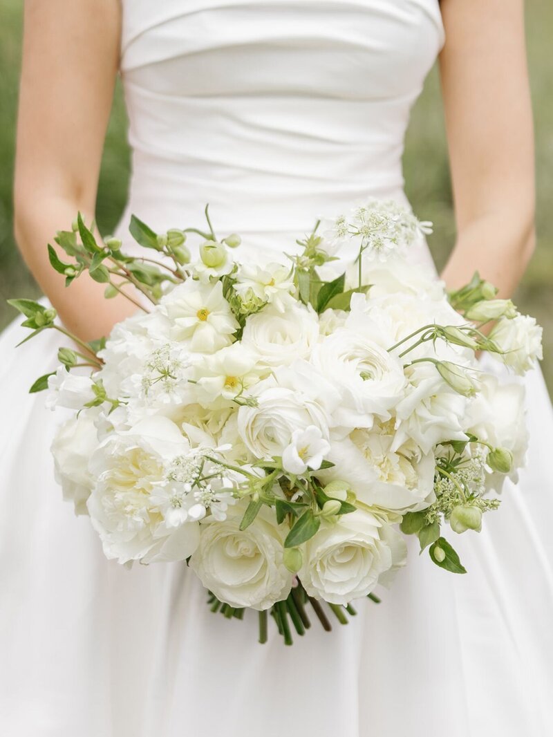 Close-up of a lush white wedding bouquet filled with roses and delicate blooms.