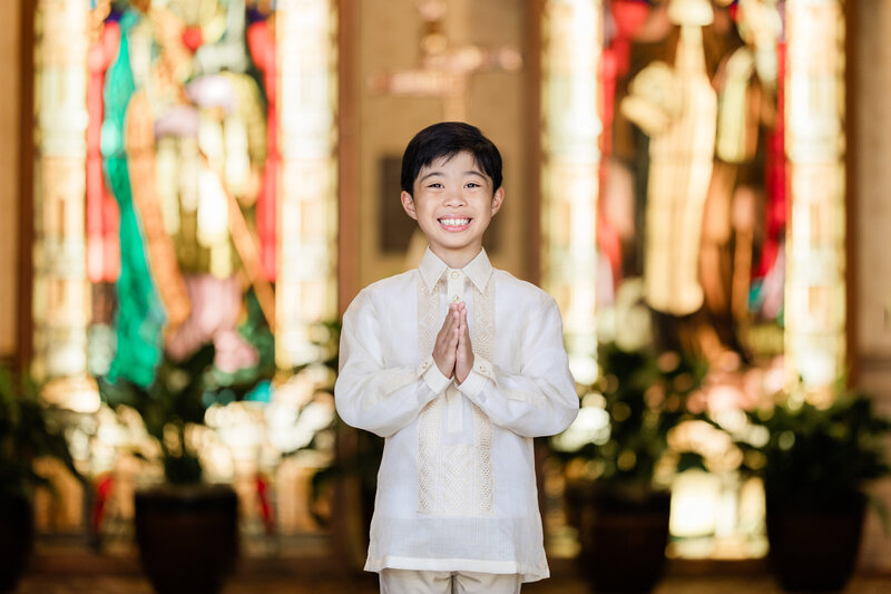 Young boy posed in front of stain glass windows in a church.