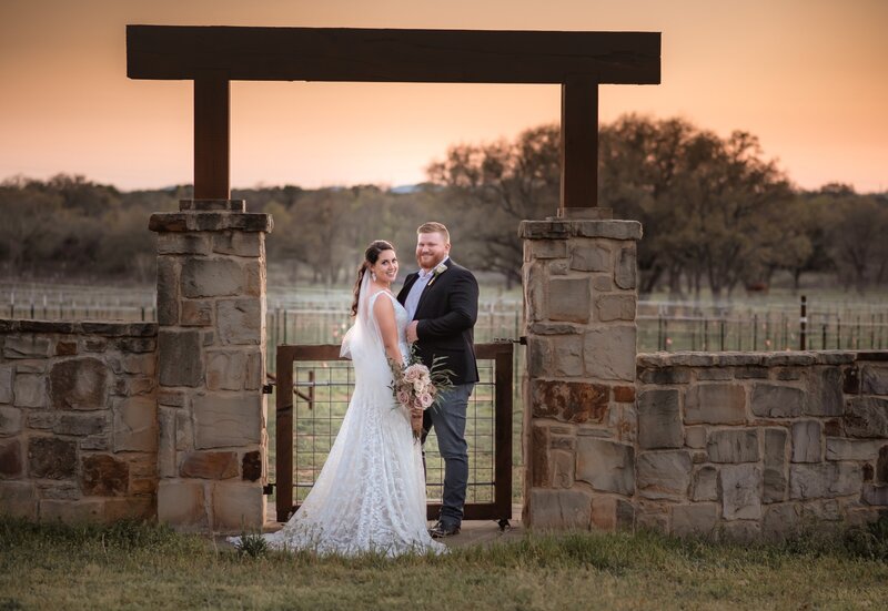 Bride and Groom standing under archway during sunset portrait in Perissos  Vineyard