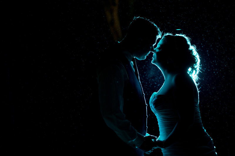 Silhouette of a couple about to kiss during a romantic nighttime rain, showcasing dramatic wedding style.