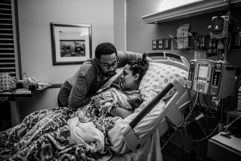 Black and white photo  of a couple lying in hospital bed with a newborn baby