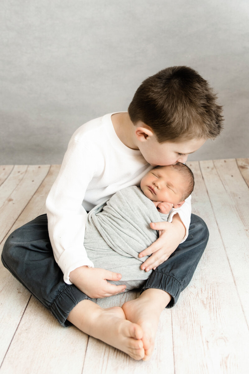 older brother kisses baby brother's head during a studio baby session
