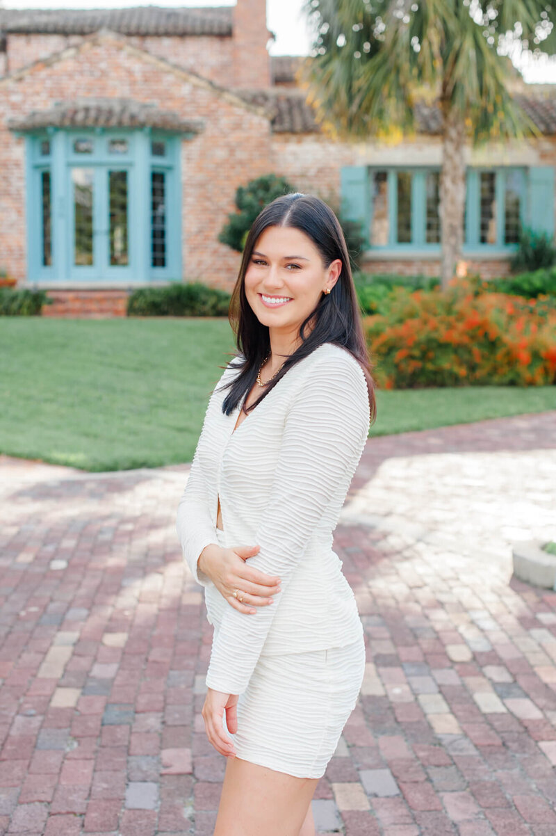 Senior girl stands in front of beautiful Casa Feliz during her Orlando senior photography session at sunset