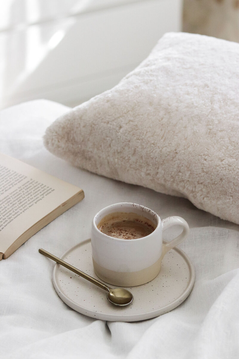 Coffee in a cup on a bed. A beige fluffy pillow in the background