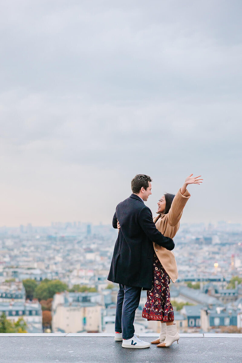 Man and woman embracing after a Paris proposal near Sacré-Cœur in Montmartre, with the woman raising her hands in excitement