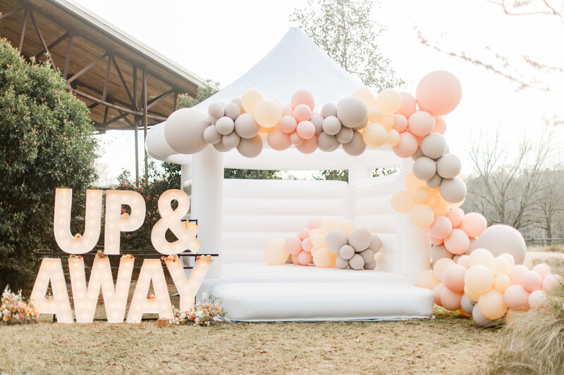 White bounce house with peach pastel balloon garland and marquee letters saying up and away