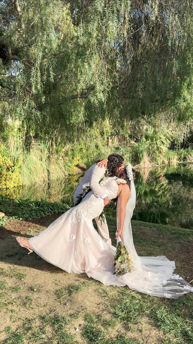 Groom dipping the bride and kissing her during their portraits by the pond at The Orchard Wedgewood Weddings in Riverside.