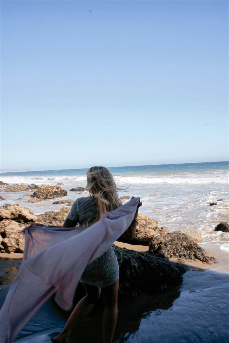 Nicky Lynn dancing on the shoreline in a blue dress, expressing freedom, joy, and emotional release
