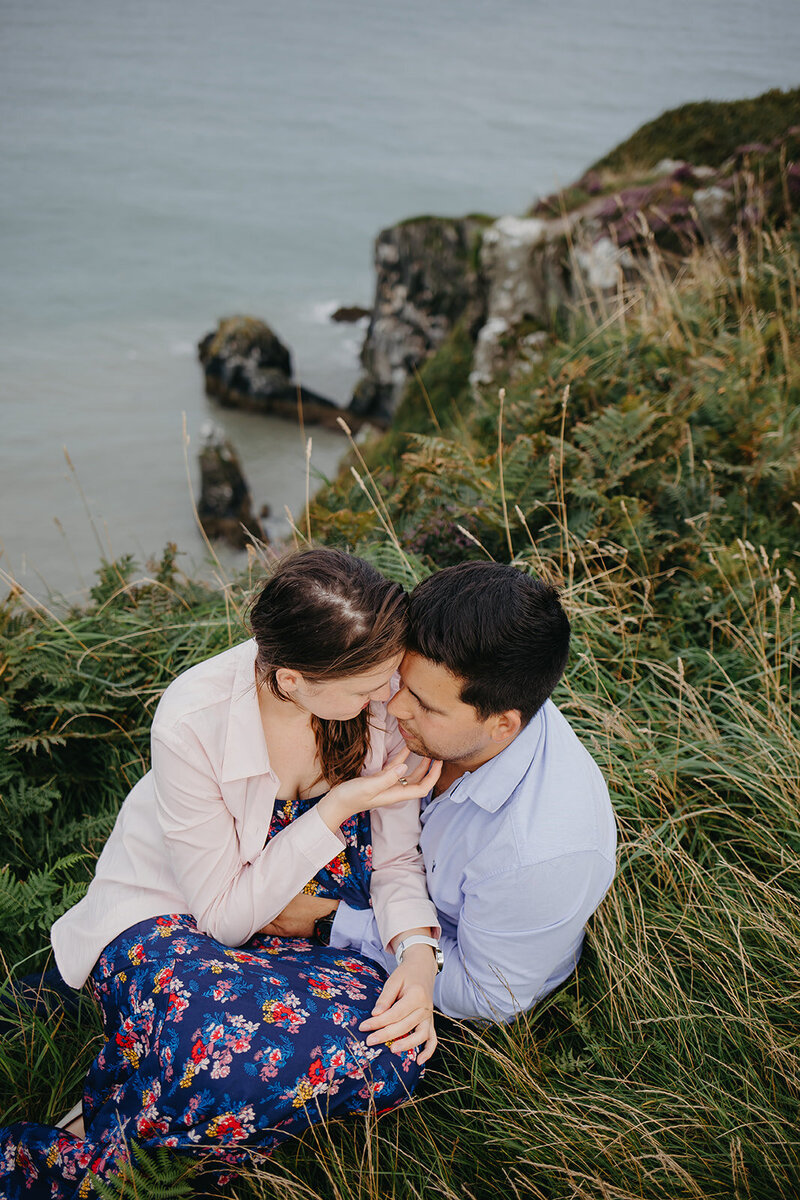 Couple photoshoot at the cliffs of Howth, sharing a quiet, romantic moment with dramatic sea views in the background.