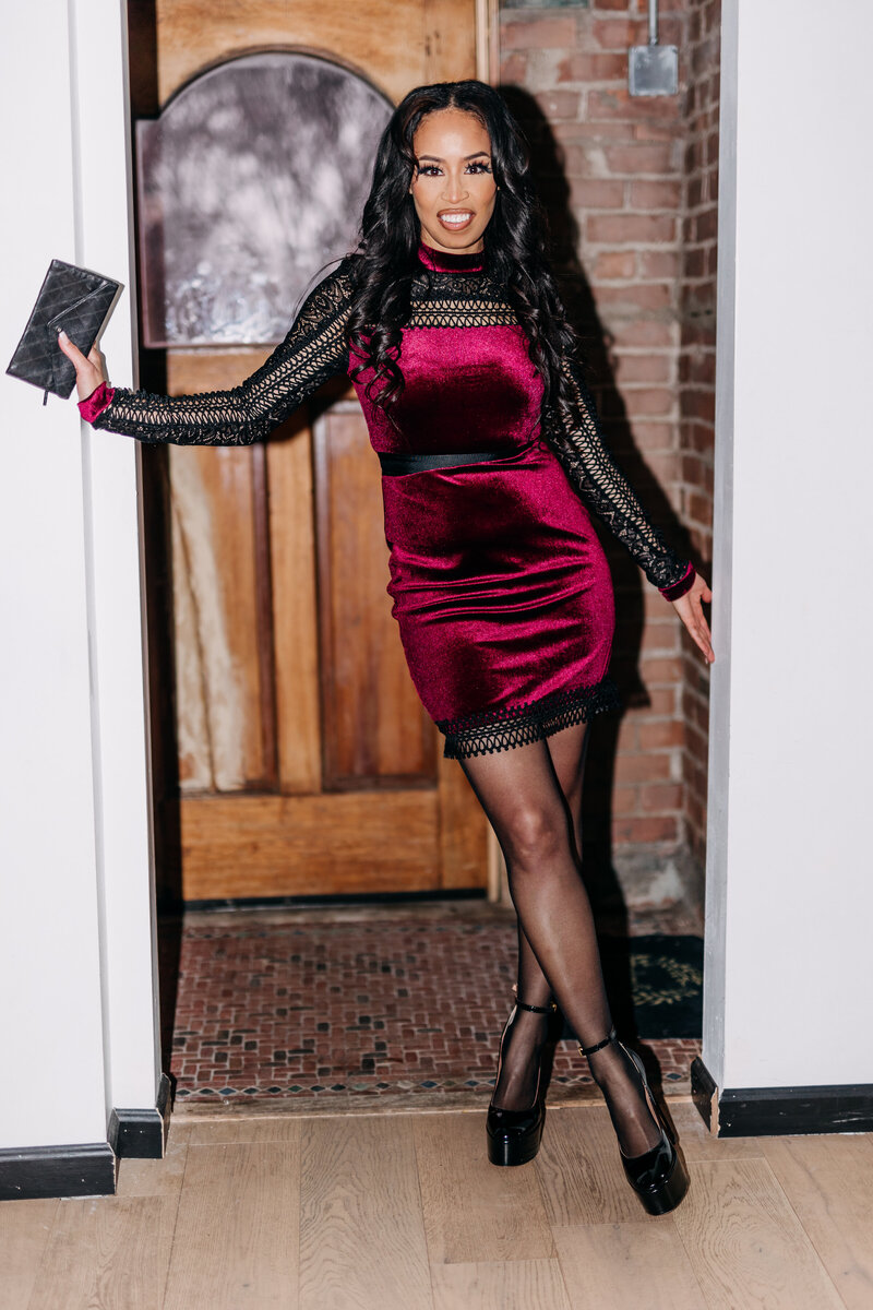 Flash photo of Tiara standing in a doorframe wearing a red and black dress and black heels