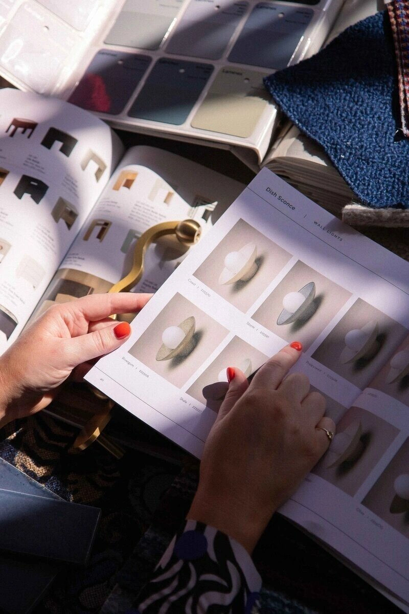 A person's hands with orange nail polish flipping through a catalog of wall sconces.