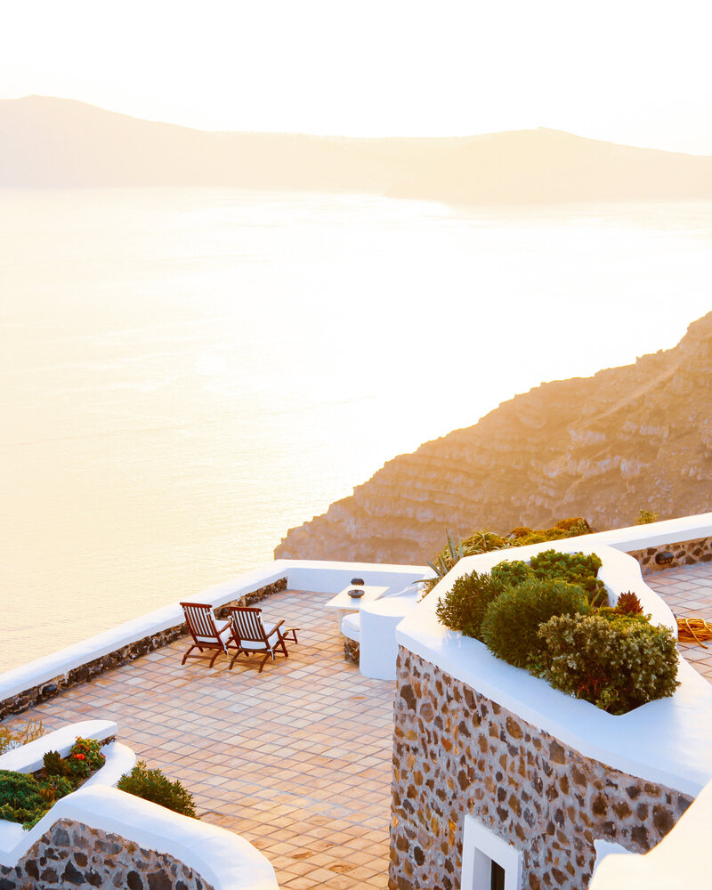 A greek stone walled terrace overlooks the sea at sunset before the wedding venue is set up.