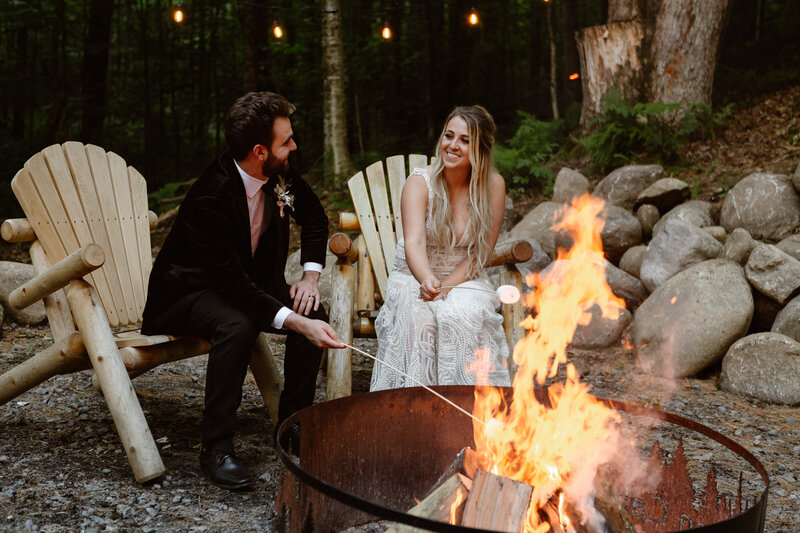 Bride and groom roast marshmellows sitting around a campfire after their upstate New York elopement.
