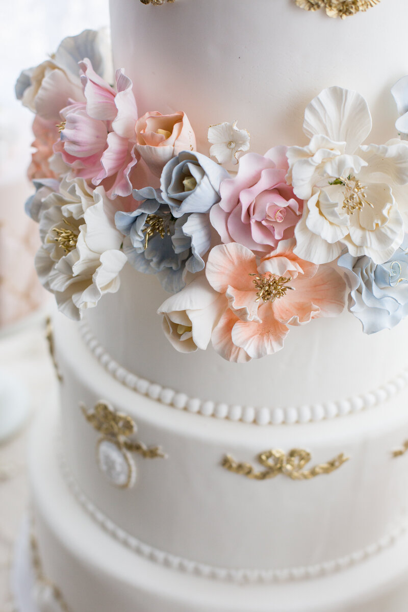A white/cream wedding cake with gold details and pastel flowers.