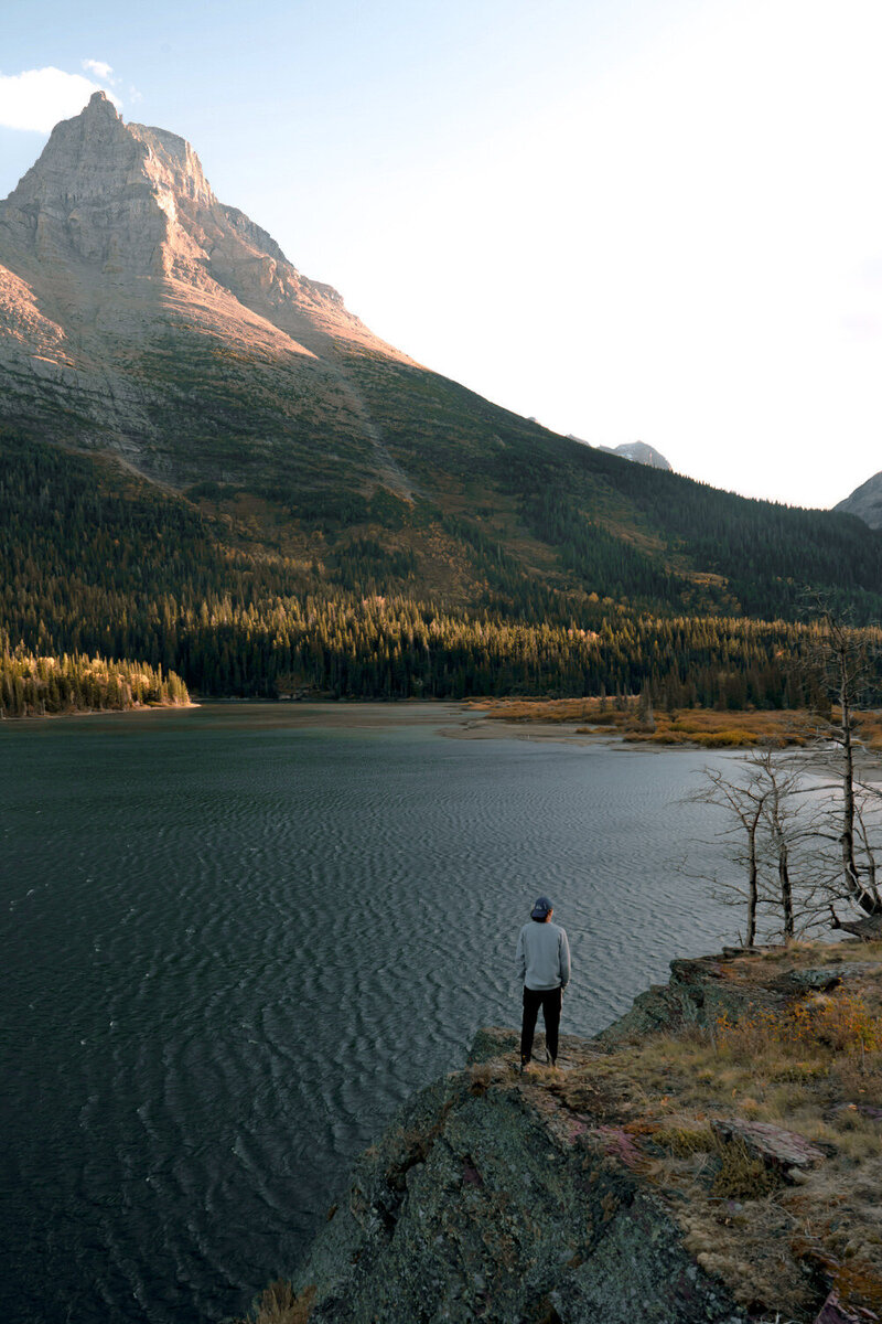Man standing on a cliff overlooking a lake with a mountain in the distance