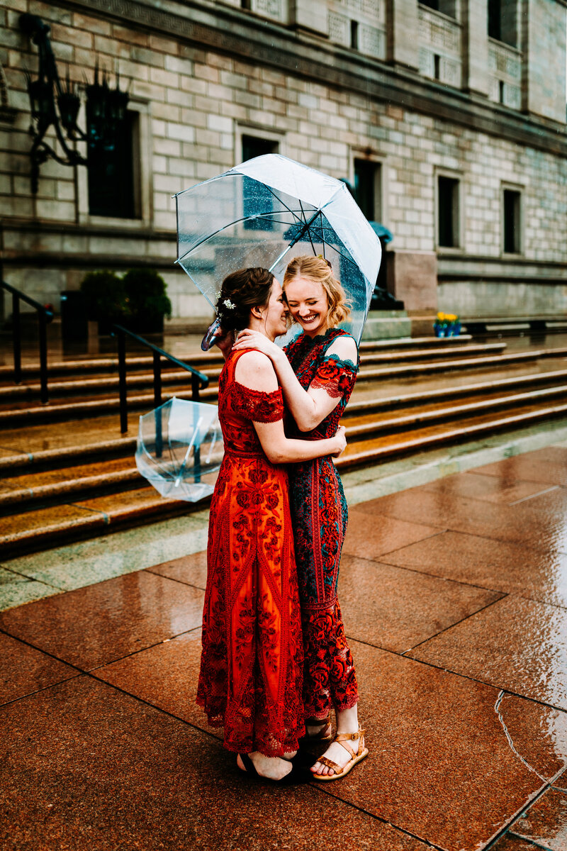 Two brides wearing red dresses in a photo taken in Boston in the rain
