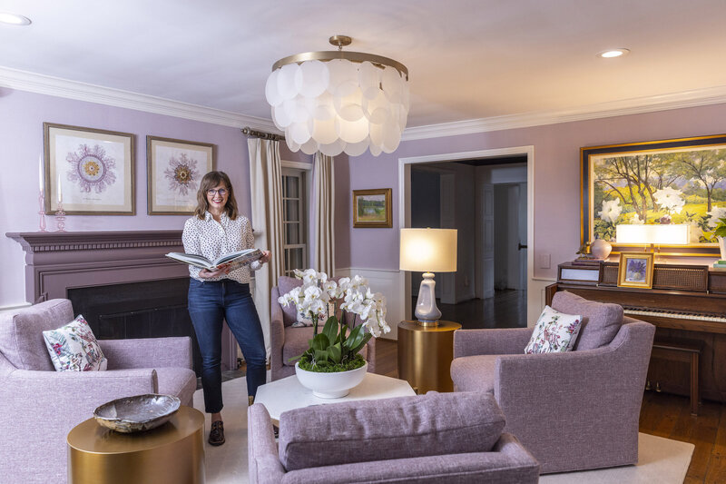 Jackie Barnes, interior designer standing in a furnished purple living room in Cincinnati.