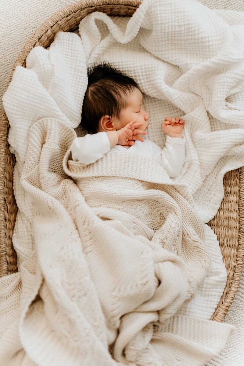 Nyfødt gutt som ligger i en kurv med tepper og sover.