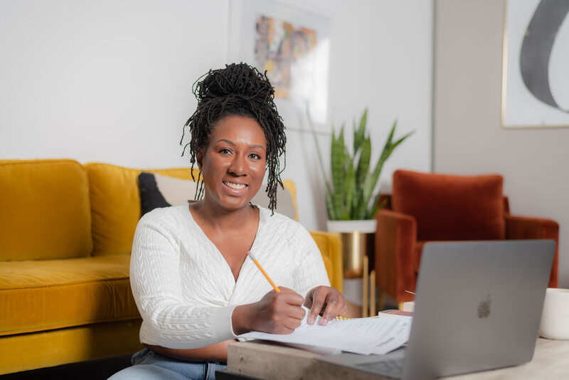brand design client sitting in front of a yellow couch holding a pencil and smiling