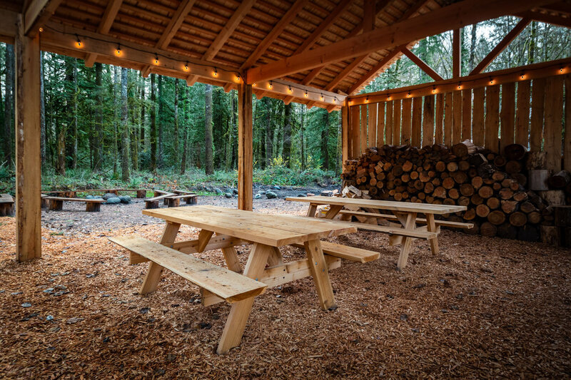 Covered picnic shelter with wooden tables and stacked firewood