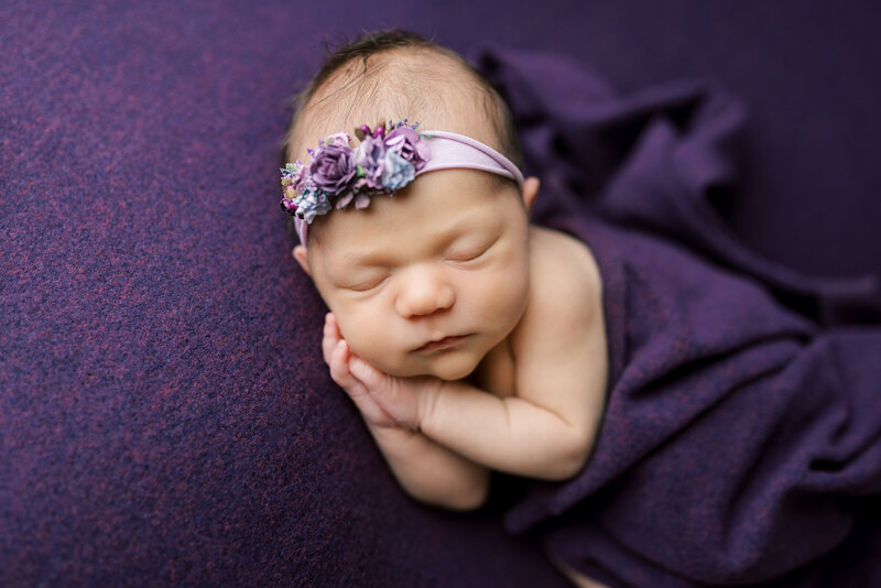 newborn with headband wrapped in purple blanket