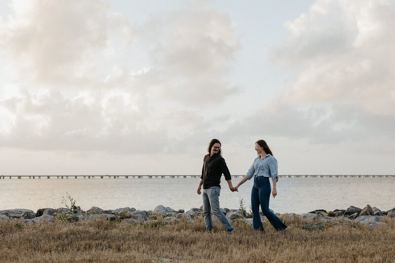A couple walks hand in hand by the water.