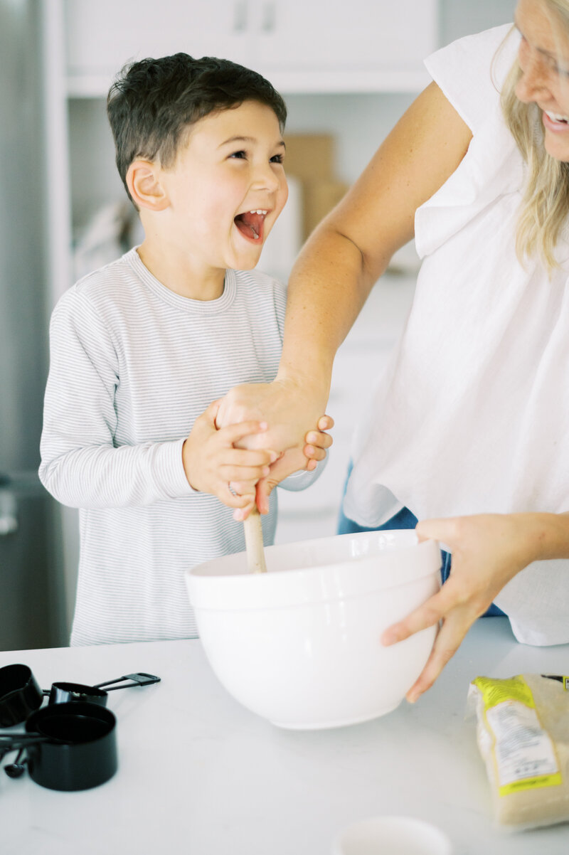 Little boy laughing and mixing food with his mother