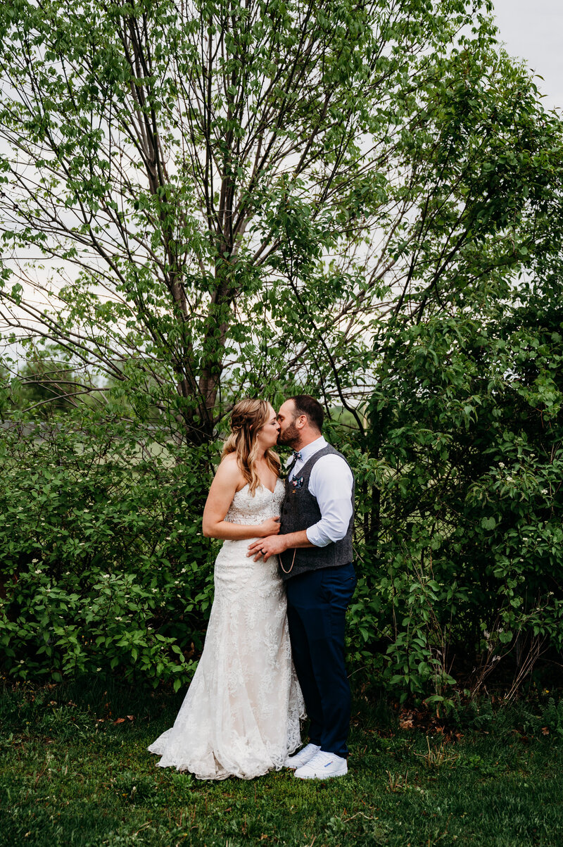 Bride and groom kissing in front of trees