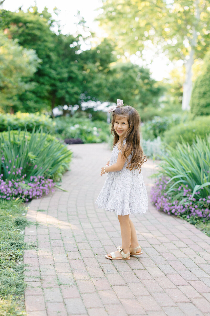 Portrait of a little girl standing on a paved pathway in a garden taken by missy marshall