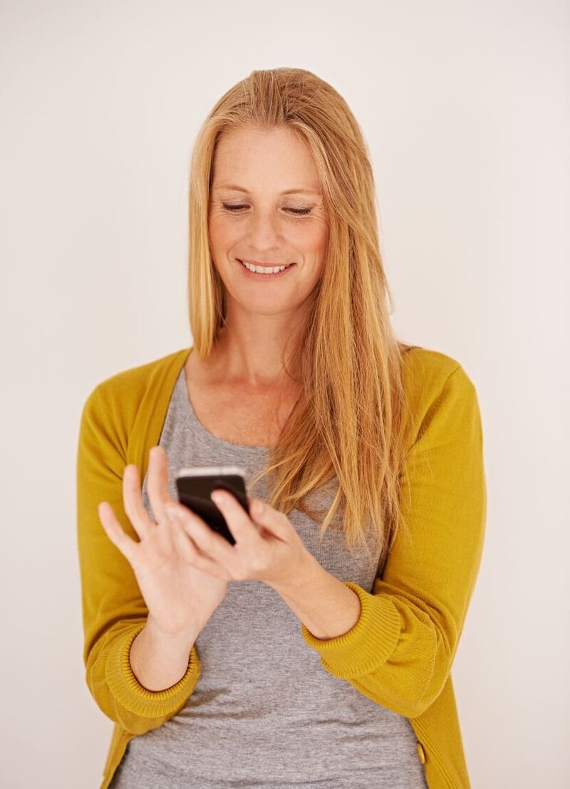 A woman smiling at her cellphone while scrolling through. This can represent a sense of resilience in surviving infidelity with our online guides.