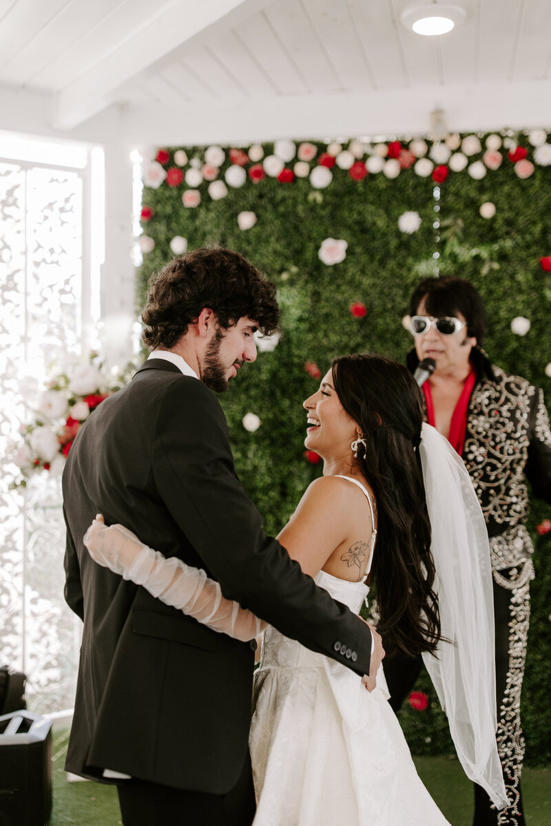 A married couple smiles at each other while an Elvis impersonator speaks into a microphone