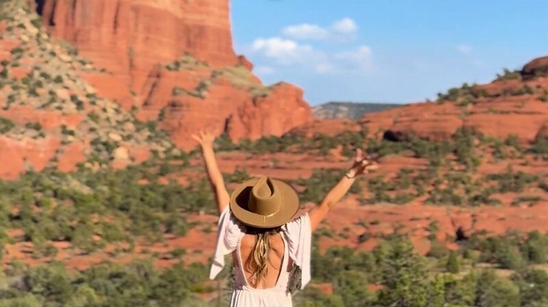 Woman with arms raised in front of Sedona red rock formations, symbolizing clarity, empowerment, and on-demand coaching support.